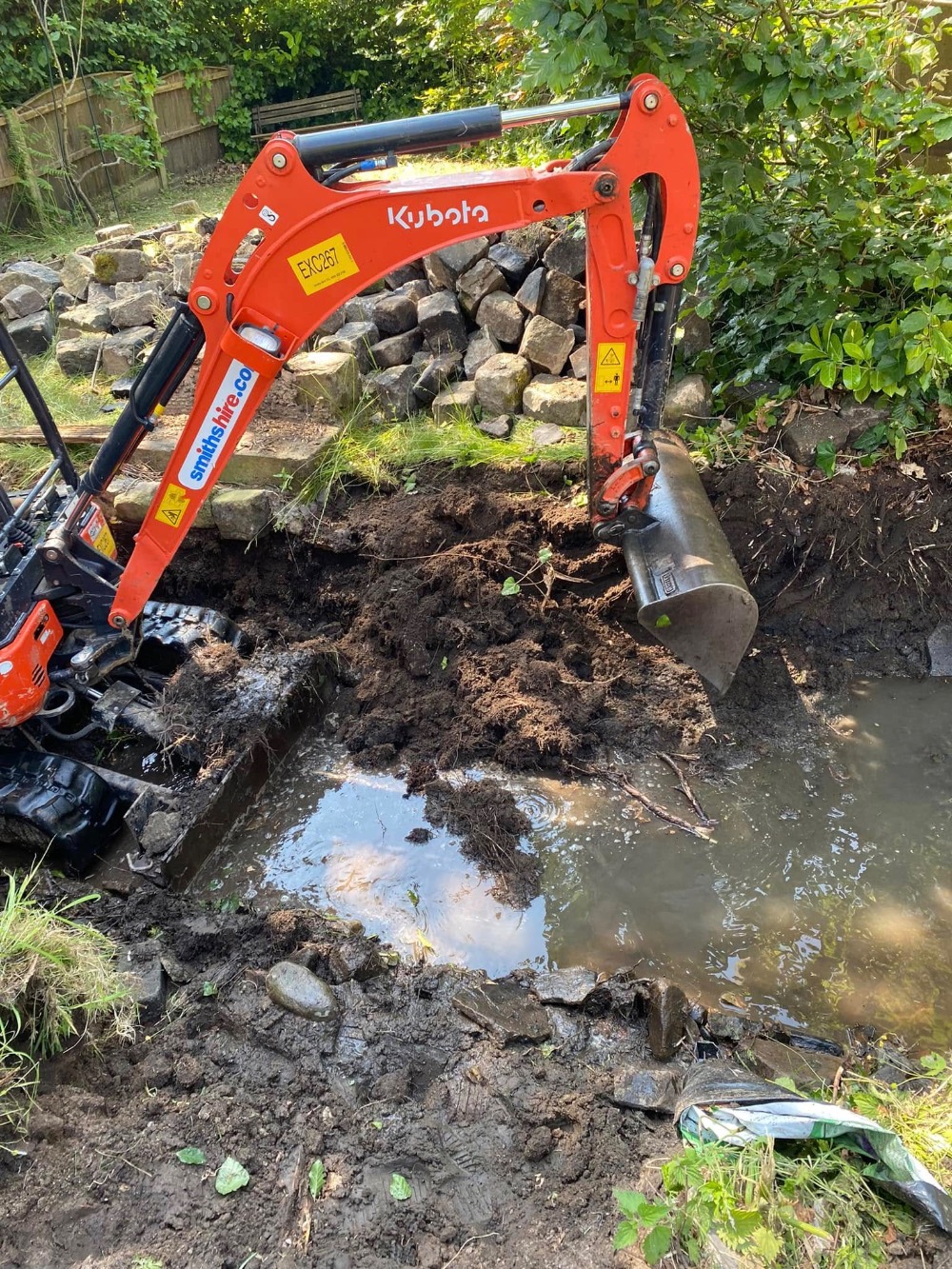 Mini excavator carrying out groundworks beside a stream