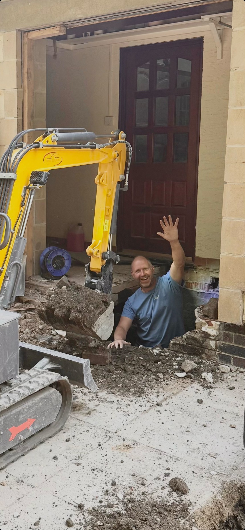 Richard from Tonge Builders waving from the groundworks of a home extension, beside the branded mini-digger